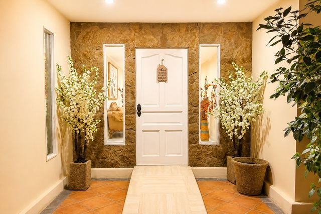 Puerta de acceso blanca flanqueada por espejos altos y maceteros con flores
