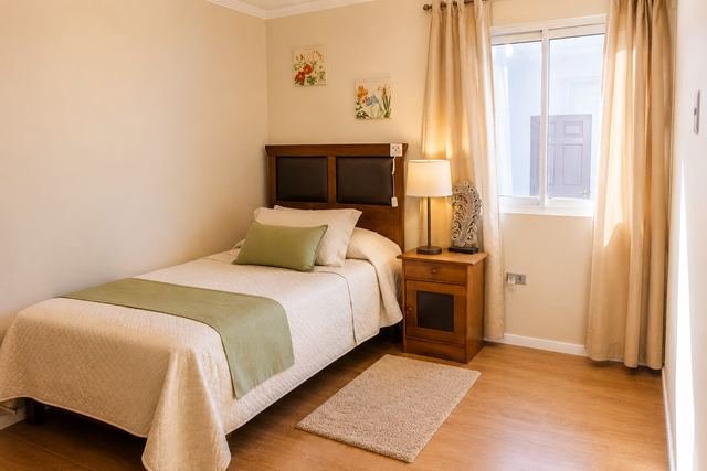Habitación individual con cama, velador, lámpara y ventana con cortinas